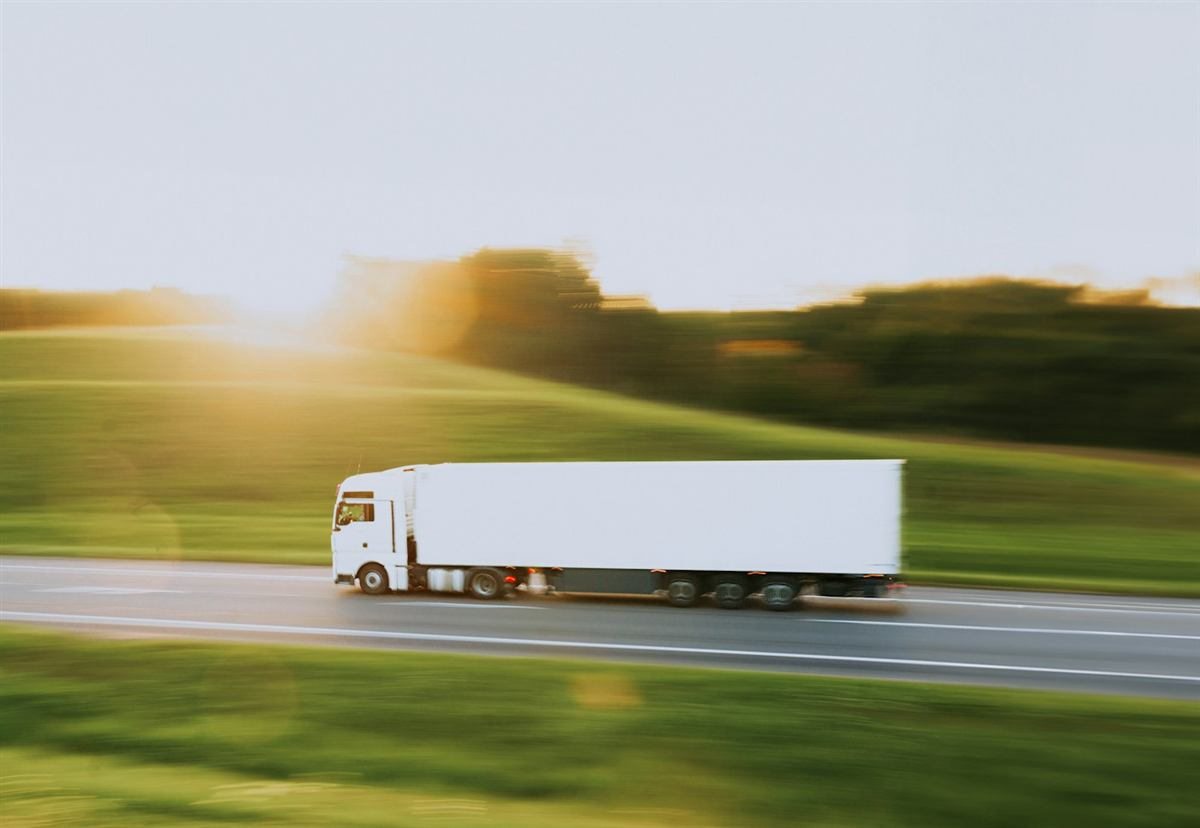 Carreta branca com baú em movimento numa rodovia